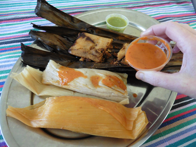 Pork and chicken tamales in corn husk wrappers (front) and chicken mole in a banana leaf wrapper (rear).