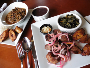 Haiti’s distinctive dish called Legume is at left, with fried plantains. At right, Griot with pikliz slaw and collard greens.