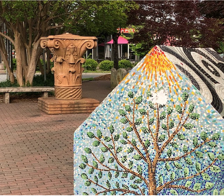 Sculptures by Paul Sires (the carved terra cotta piece that looks like the capital of a Corinthian column) and Ruth Ava Lyons (the mosaic walls and 'house') made this spot a point of pride in 1994 – a key step in the rebirth of this then-neglected business district. 

Sires and Lyons ran Center of the Earth gallery on North Davidson Street in those years, which sparked the revitalization of Charlotte's NoDa neighborhood.