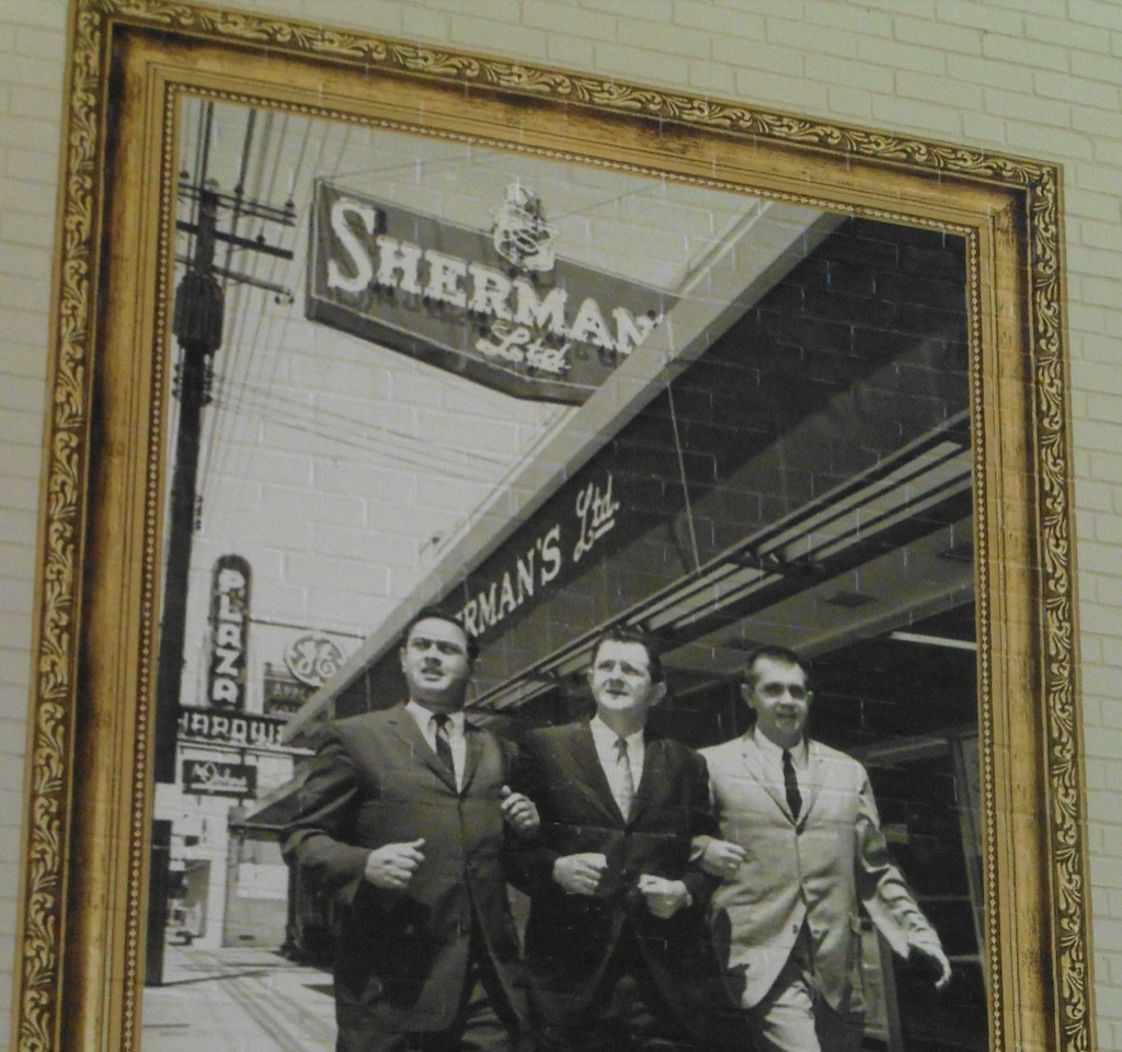 Look up on the wall to see a giant 1960 photo of brothers Sherman, Alvin, and Leon Levine. They’d just launched Sherman’s Ltd. (a beloved clothing shop, now site of Midwood Guitars), Pic ’n Pay Shoes (soon to become a major national chain), and Family Dollar (now a coast-to-coast discount chain)— all in the 1500 block of Central Avenue. Image from Charlotte Mecklenburg Library’s Carolina Room.